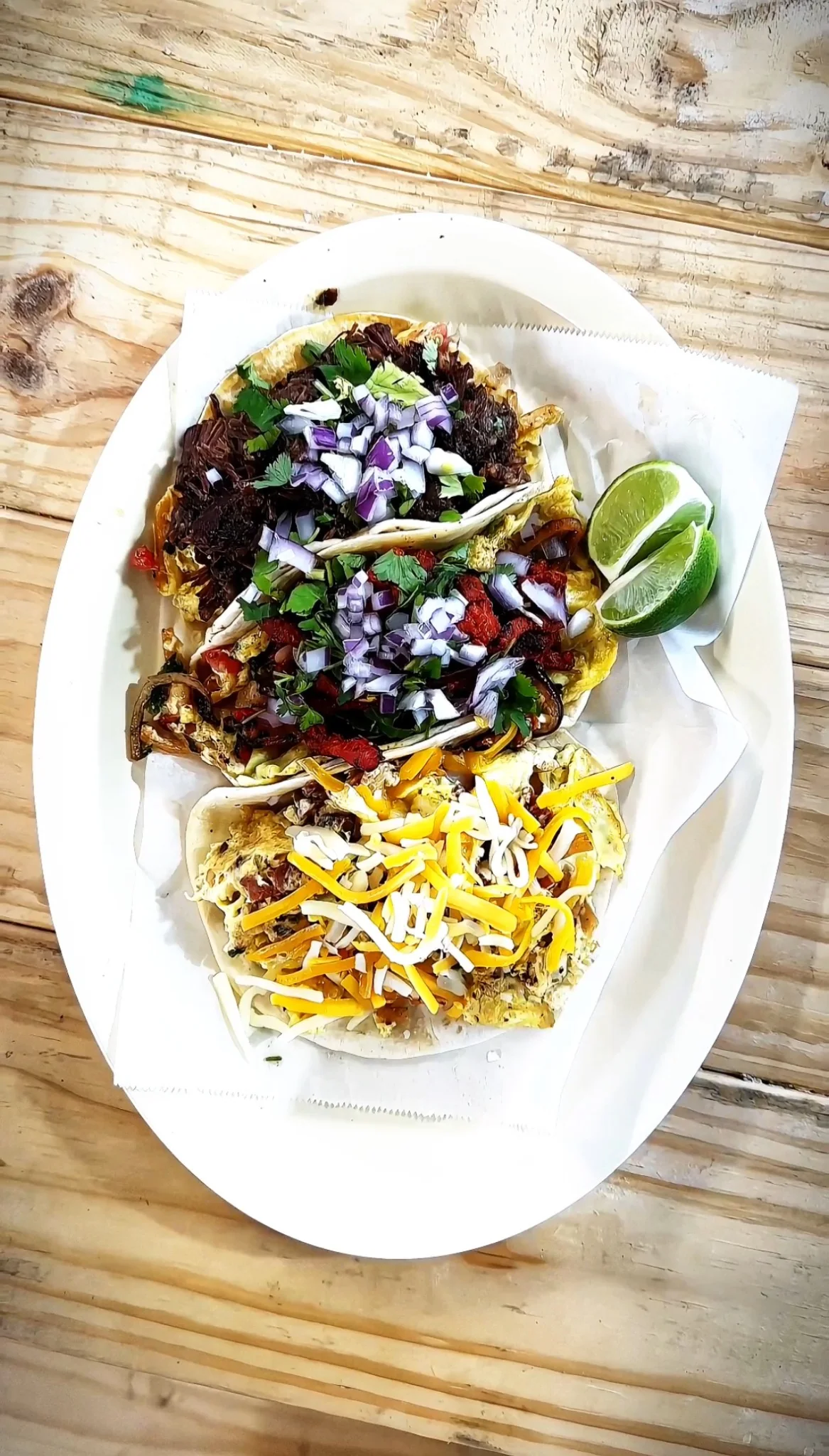 Three tacos with onions, cilantro, cheese and lime