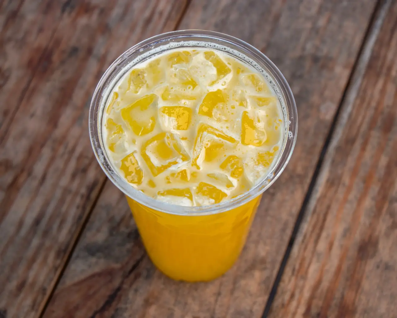 Golden agua fresca served over ice on a wooden table.