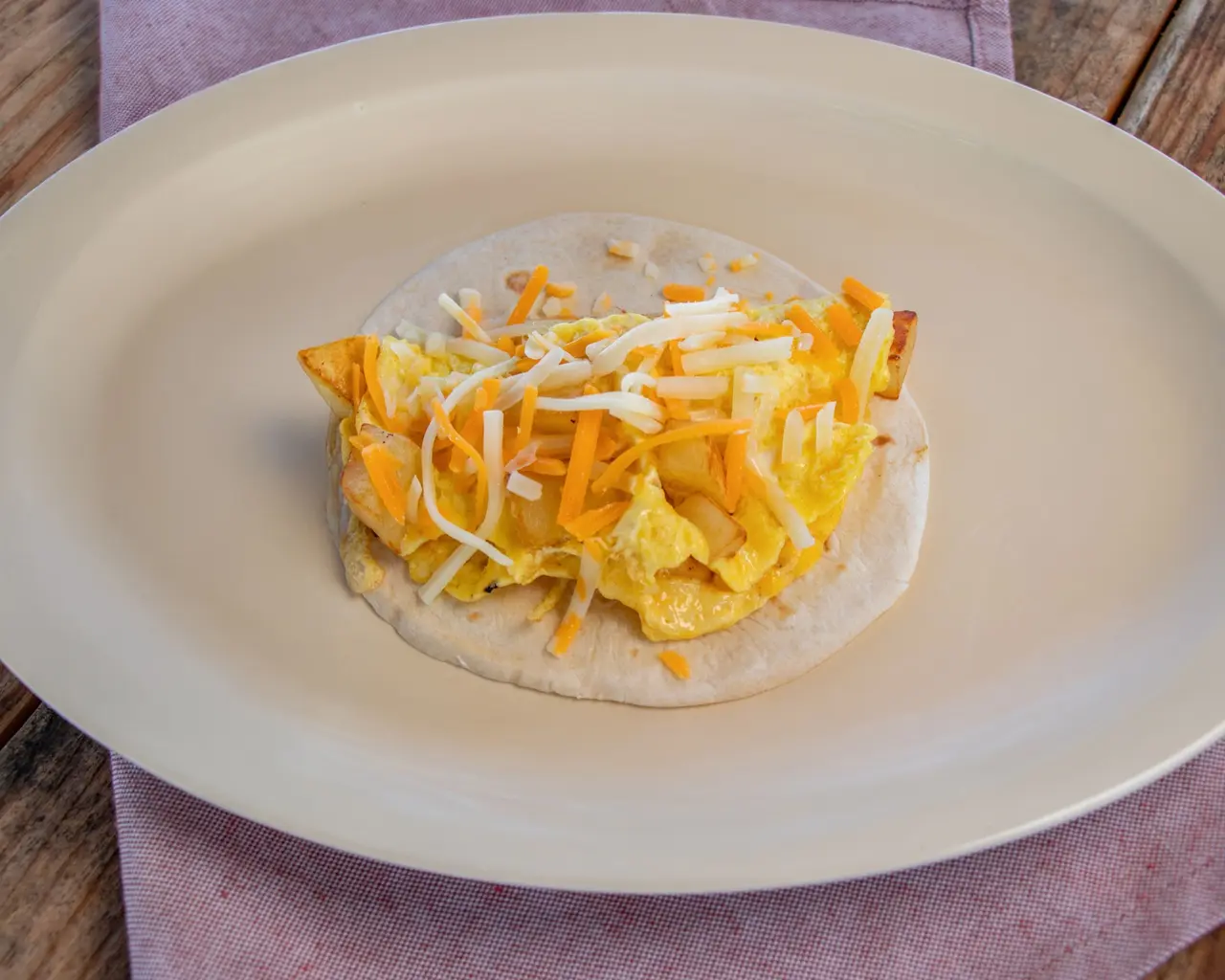 Breakfast taco with eggs, potatoes and shredded cheese on a cream plate.