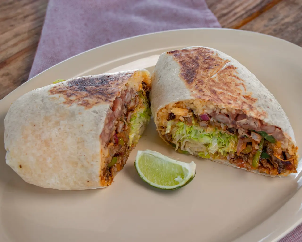 Griddled burrito cut open to show rice, beans, lettuce and meat.