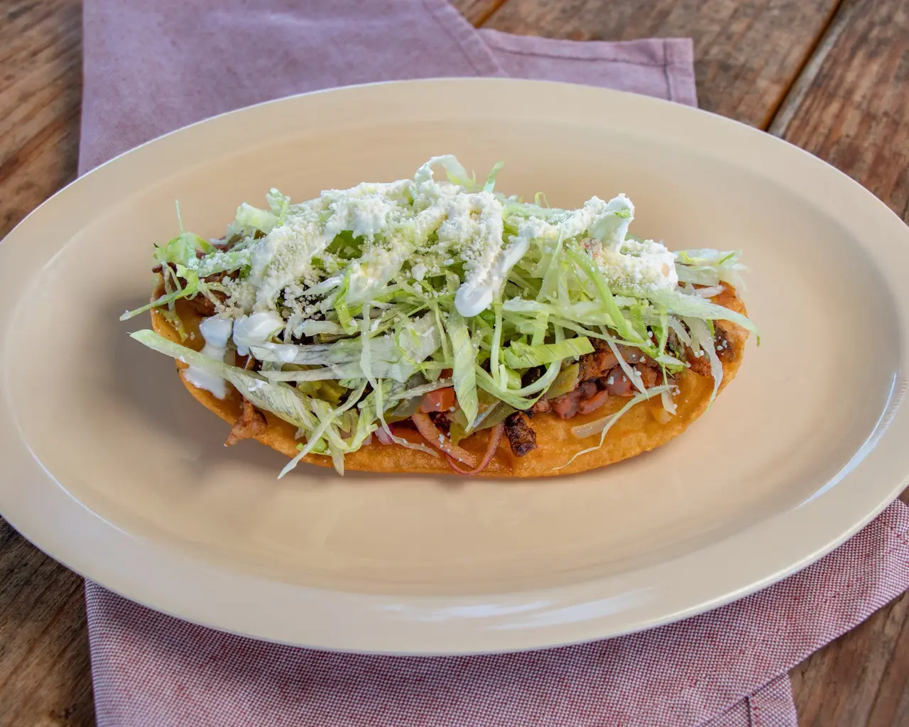 Huarache topped with meat, lettuce, crema and crumbled cheese.