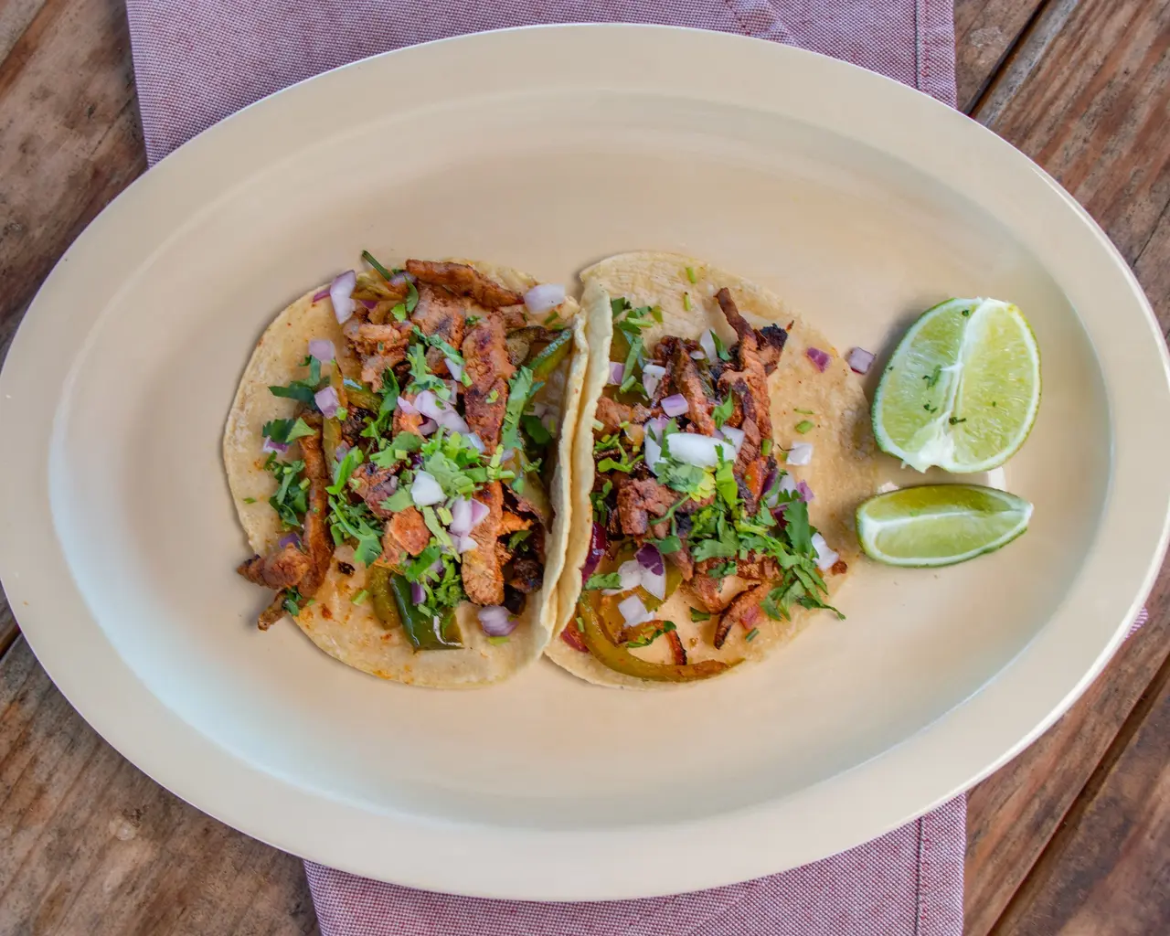 Two tacos with grilled meat, peppers, onions, cilantro and lime.