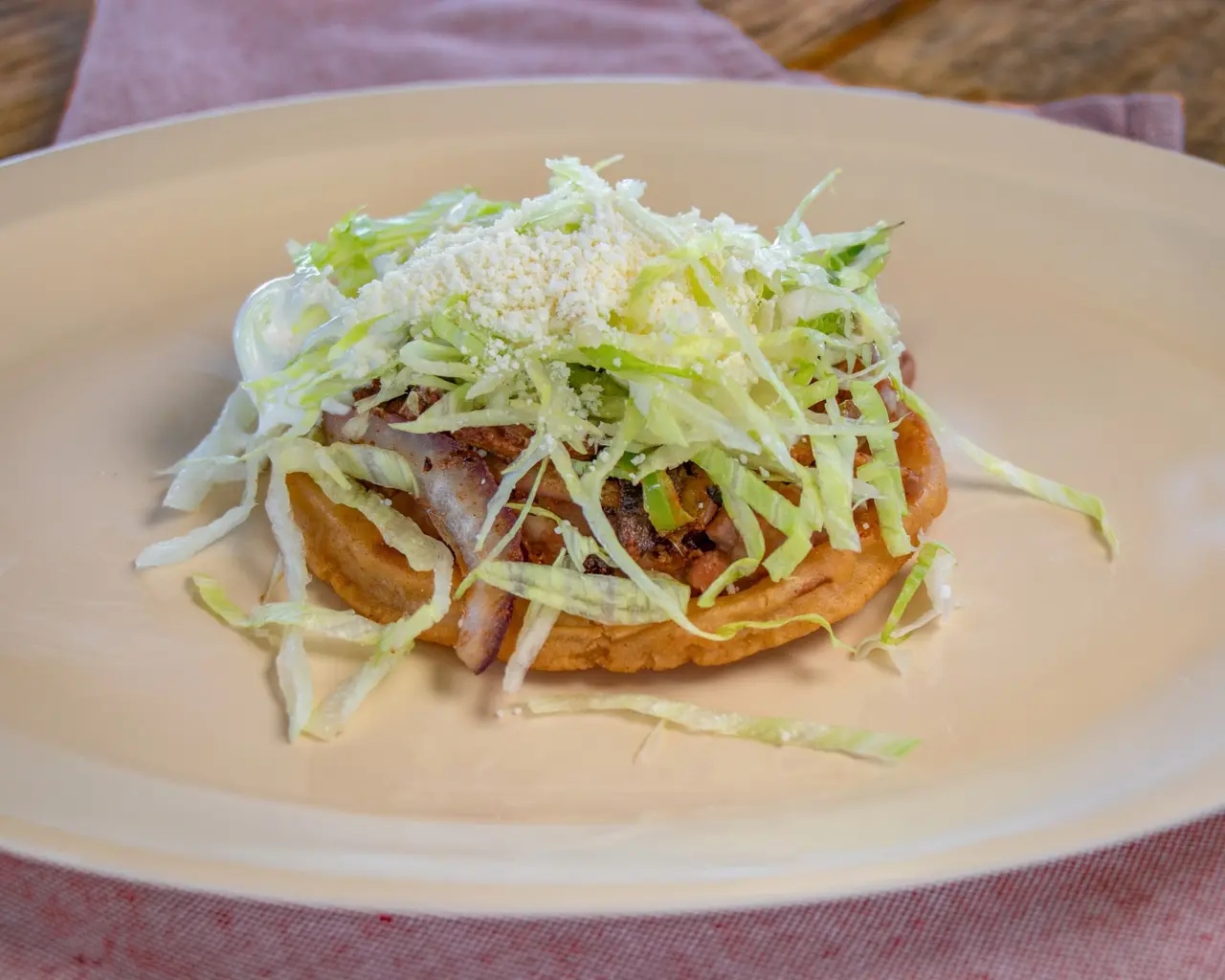 Sope topped with meat, lettuce, crema and crumbled cheese.